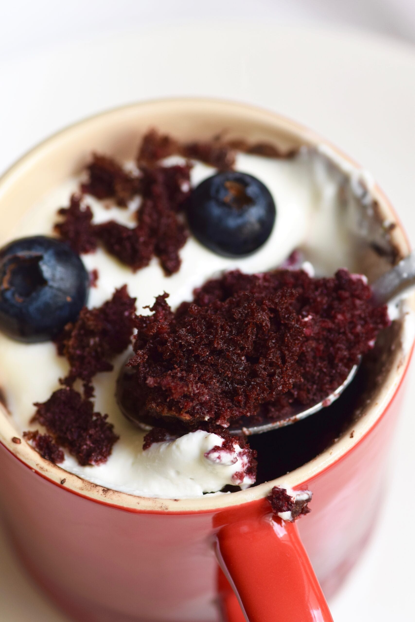 Healthy red velvet cupcake mug cake with cheesecake frosting and blueberries