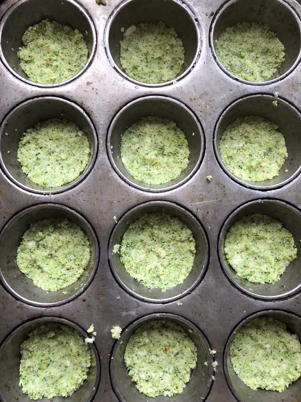 Placing mini cauliflower pizza dough into muffin tin