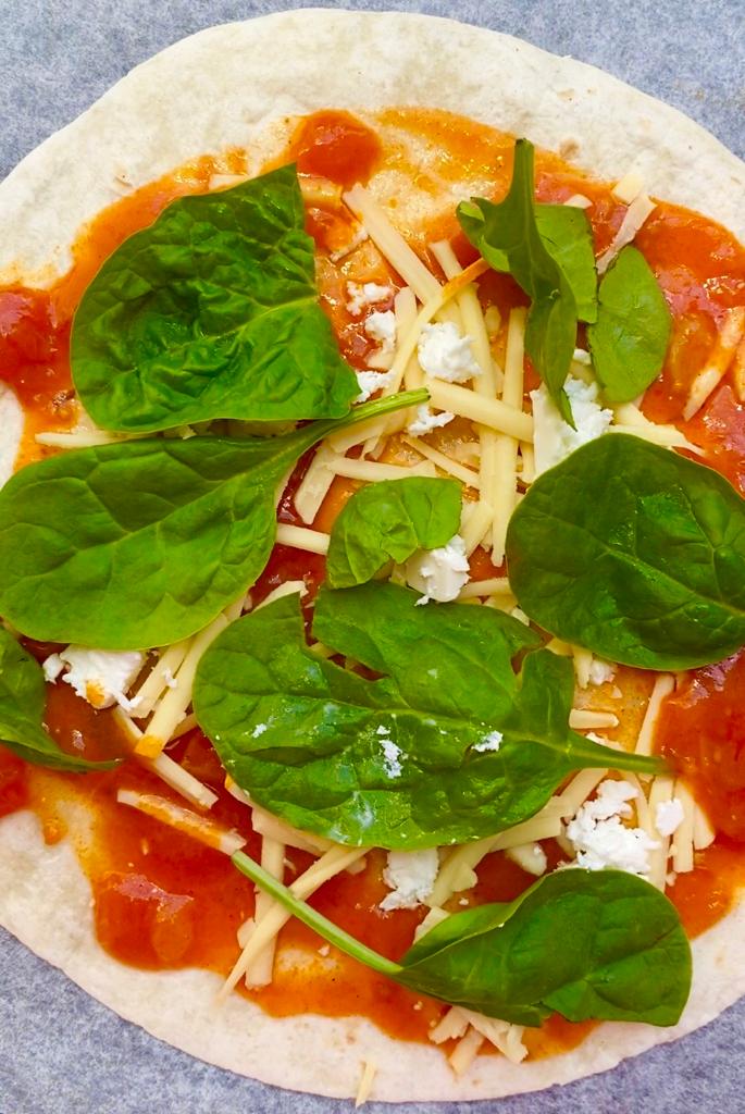 Topping tortilla with crushed tomato, cheese, spinach & feta